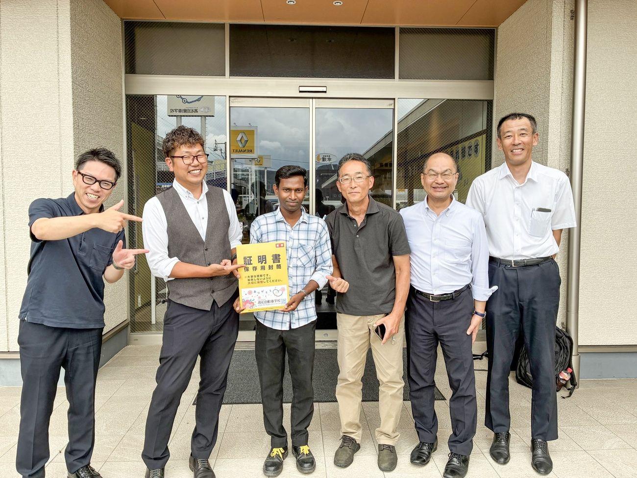 Masidas with his instructors at his driving school in Japan, licence certificate in hand